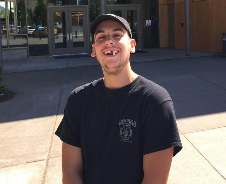 REFLECTING POSITIVELY: Senior Tage Baumgartner flashes a toothy smile in front of the school where he spent the last four years of his life. “I’m really glad I joined iVision this year to teach the kids how to cook,” he says.